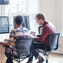 A man and woman working at a desk with computer monitors
